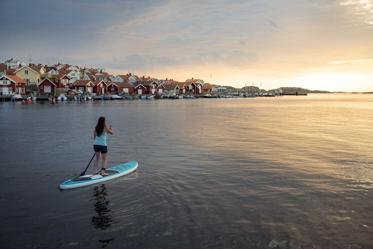 hvordan velge rett padleboard: en kvinne ved en innsjø står på et brett