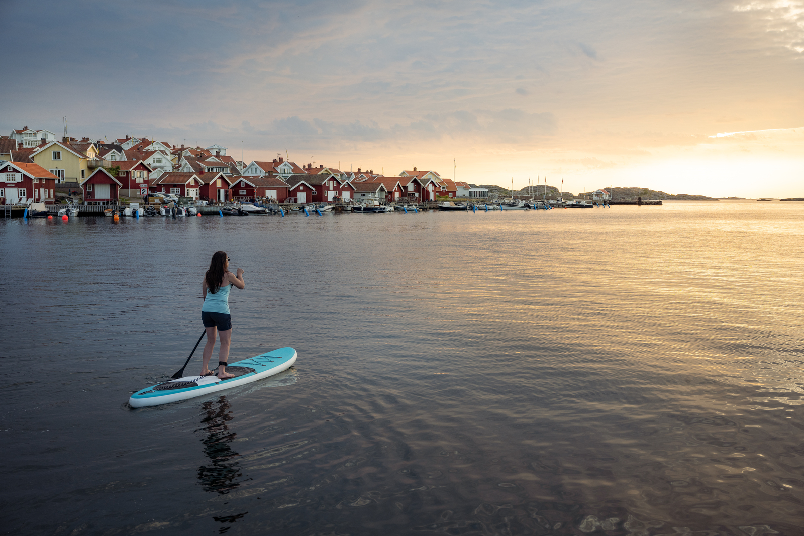 hvordan velge rett padleboard: en kvinne ved en innsjø står på et brett